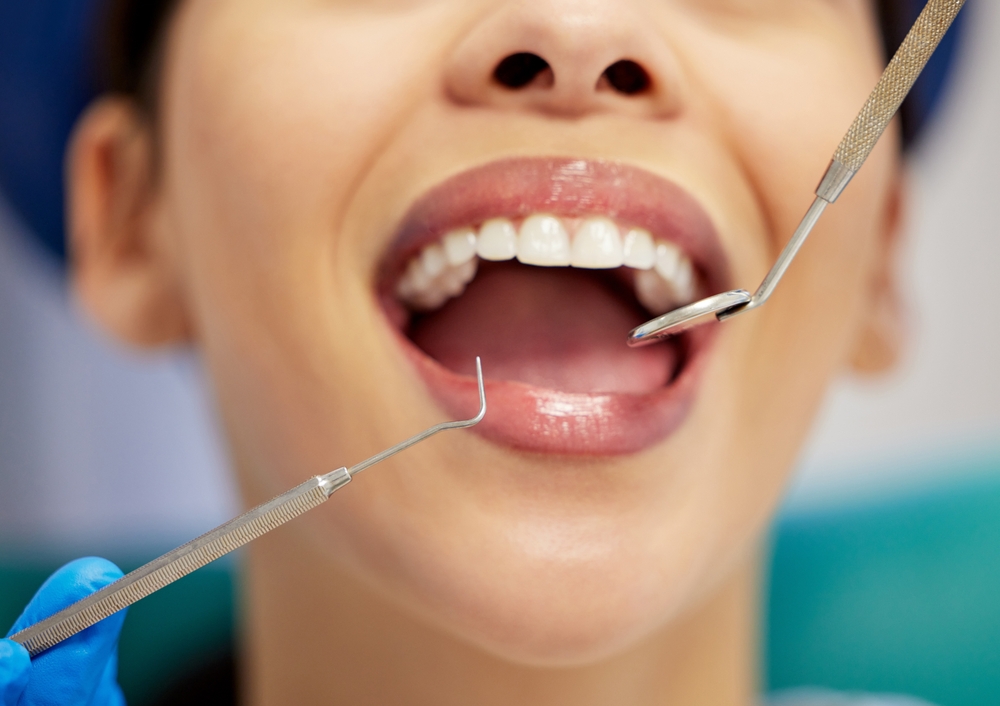A kind, male dentist wearing a white coat is holding the hand of a nervous female patient in the dental chair. No text on image.