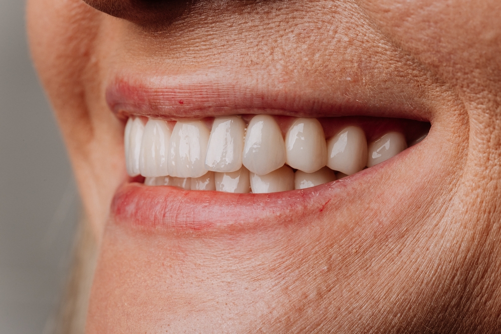 A friendly dentist in Williston, ND, wearing a white coat, smiles reassuringly at a patient in the dental chair. The background is a modern, clean dental office setting. No text on the image.