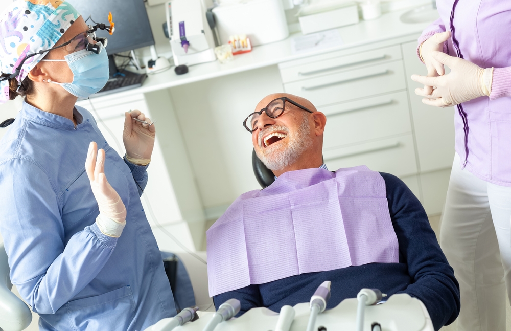 A friendly dentist in Williston, ND, is smiling and shaking hands with a new patient in a modern, clean dental office. No text on image.